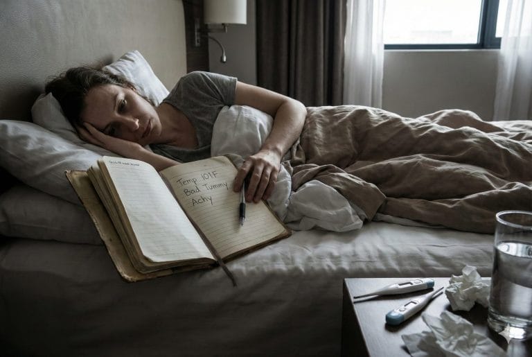 A traveler sick in their hotel room but still making a few important notes in her journal.